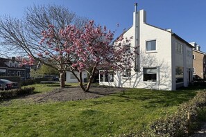 Ein modernes, zweistöckiges Haus mit weißer Fassade, einem Schornstein und einem Baum mit rosa Blüten im Vorgarten.