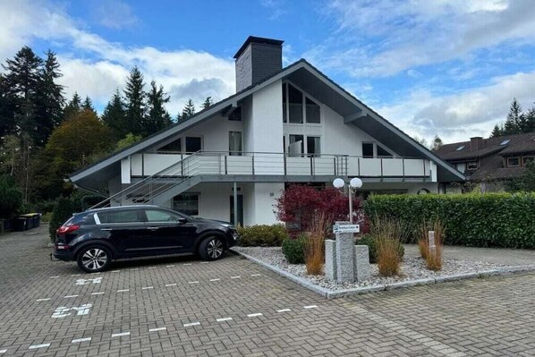 A modern building with a covered entrance, a car parked in front, and a sign indicating a business center. - No. 16 - Winterhaldenweg 37 (Hinterzarten)