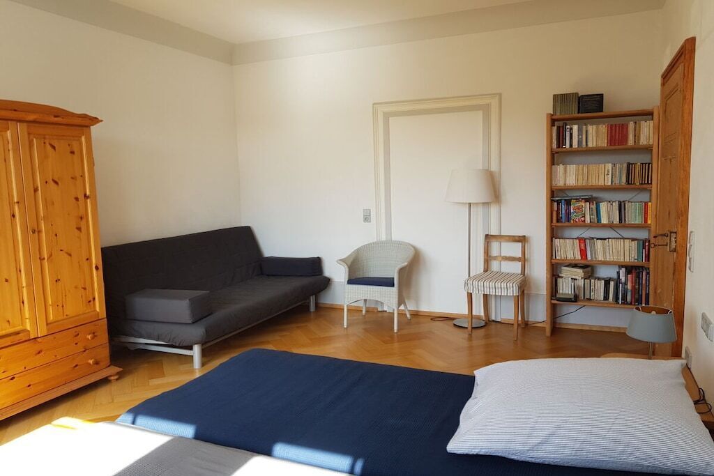 Ein Zimmer mit einem Bett, einer Couch, einem Sessel, einem Bücherregal und einem Holzschrank.