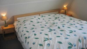 Quarto com cama, duas luminárias laterais e cabeceira de madeira.