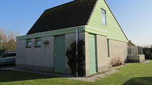 Um pequeno edifício térreo com telhado inclinado, porta verde e janela pequena.