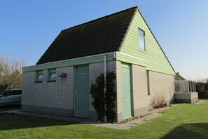 A small, single-story building with a sloped roof, a green door, and a small window. - Holiday home with 3 bedrooms (Julianadorp)