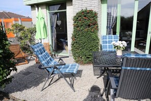 An outdoor seating area with a table and chairs, a green umbrella, and a hedge with red flowers. - Holiday home with 3 bedrooms (Julianadorp)