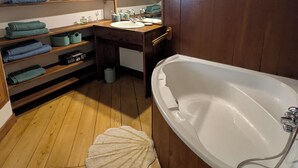 Une salle de bain avec un meuble-lavabo en bois, une grande baignoire et des étagères où sont rangées les serviettes et les articles de toilette.