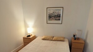 Une chambre à coucher avec un lit, deux tables de chevet, une lampe fixée au mur et un tableau encadré.