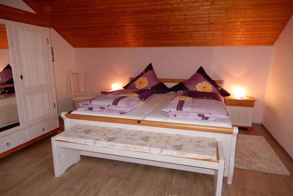 A bedroom with a wooden ceiling, a bed with floral bedding, a bedside table, and a nightstand with a lamp.