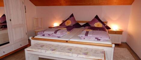 A bedroom with a wooden ceiling, a bed with floral bedding, a bedside table, and a nightstand with a lamp.
