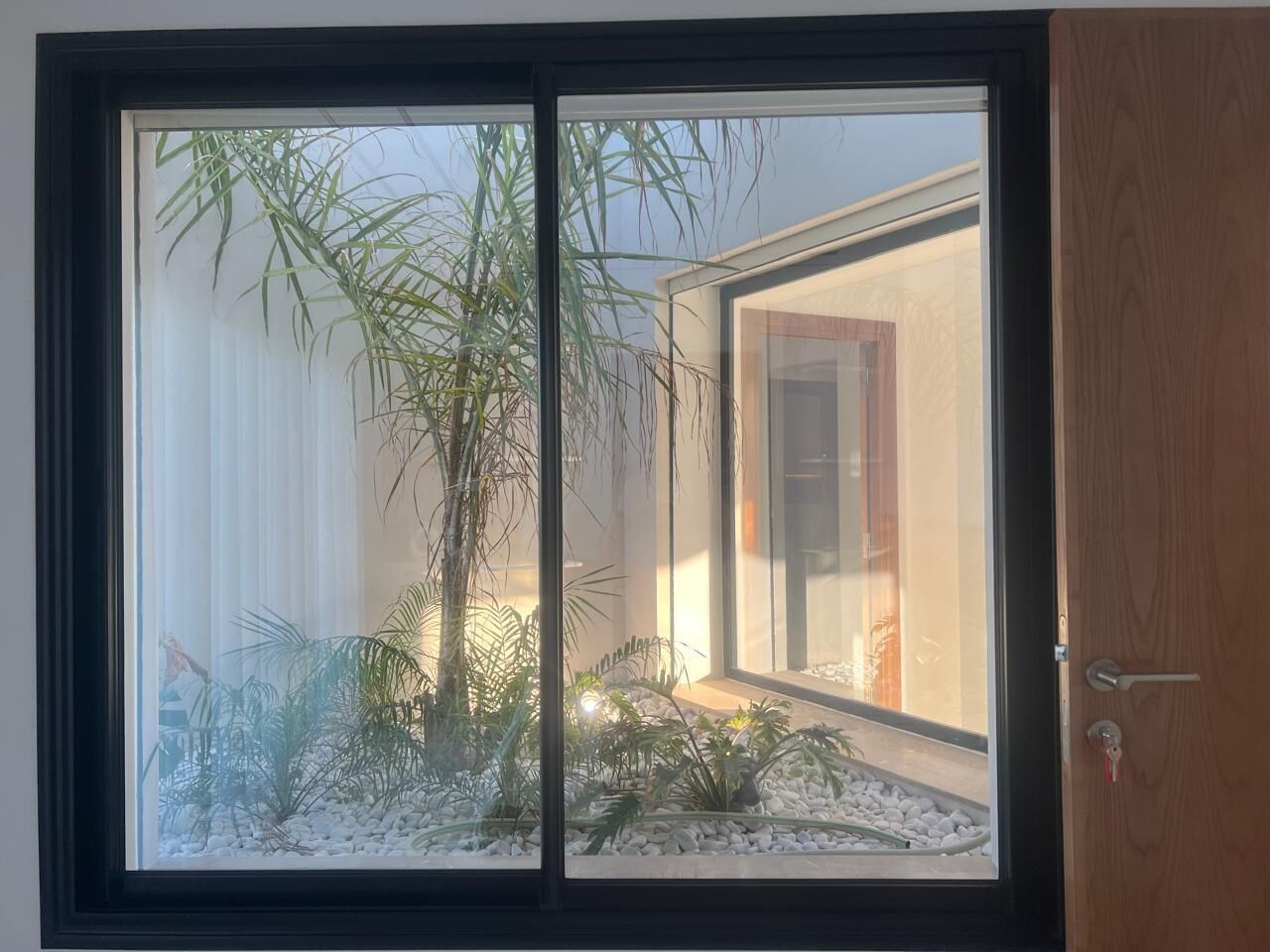 Una habitación con un ventanal grande, una puerta y un pequeño jardín interior.