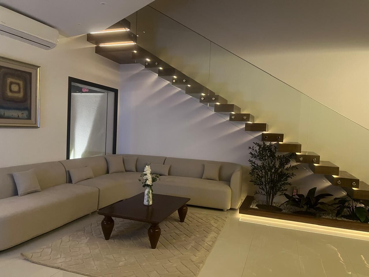 Un salon moderne avec un canapé, une table basse et un escalier doté de rampes en verre.