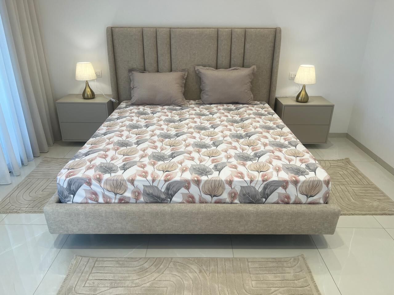 Una cama con colcha estampada, dos lámparas de noche y un cabecero.