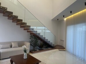 Una sala de estar moderna con una escalera de cristal, un sofá, una mesa de centro y una planta.