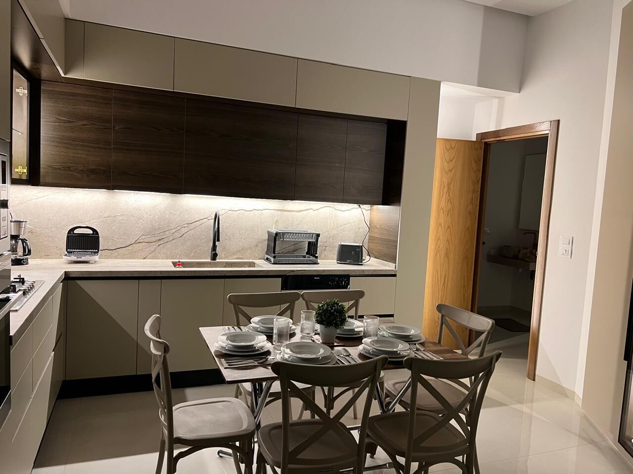 A modern kitchen with a dining area, featuring a built-in oven, a coffee machine, and a dining table set for six.