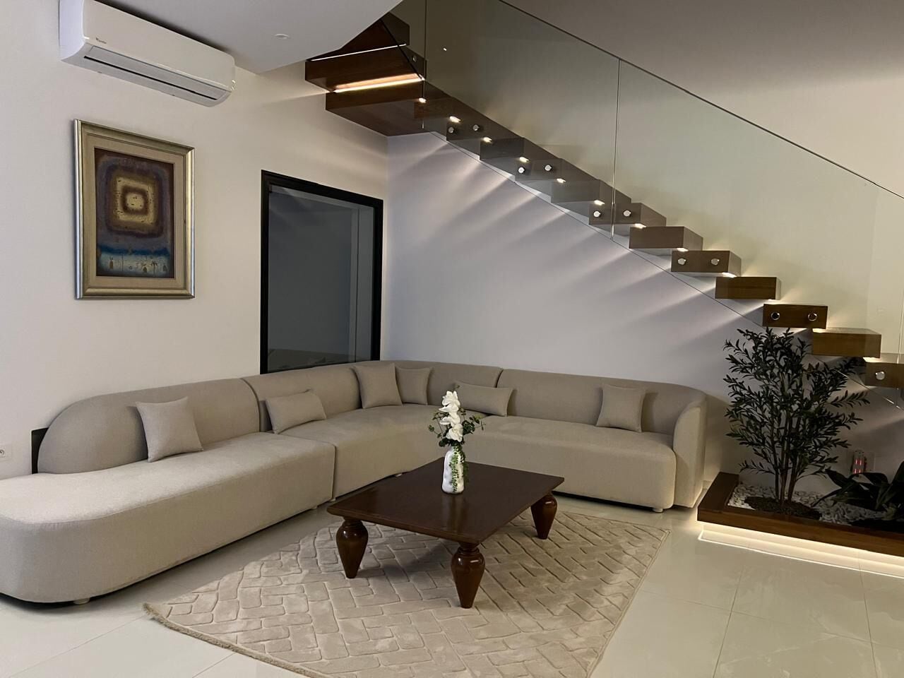 Una sala moderna con un sofá modular, una mesa de centro y una escalera con iluminación integrada.