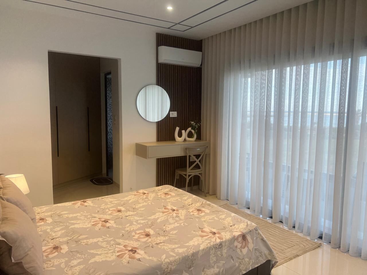Une chambre à coucher avec un lit, un bureau, une chaise et une grande fenêtre avec des rideaux.