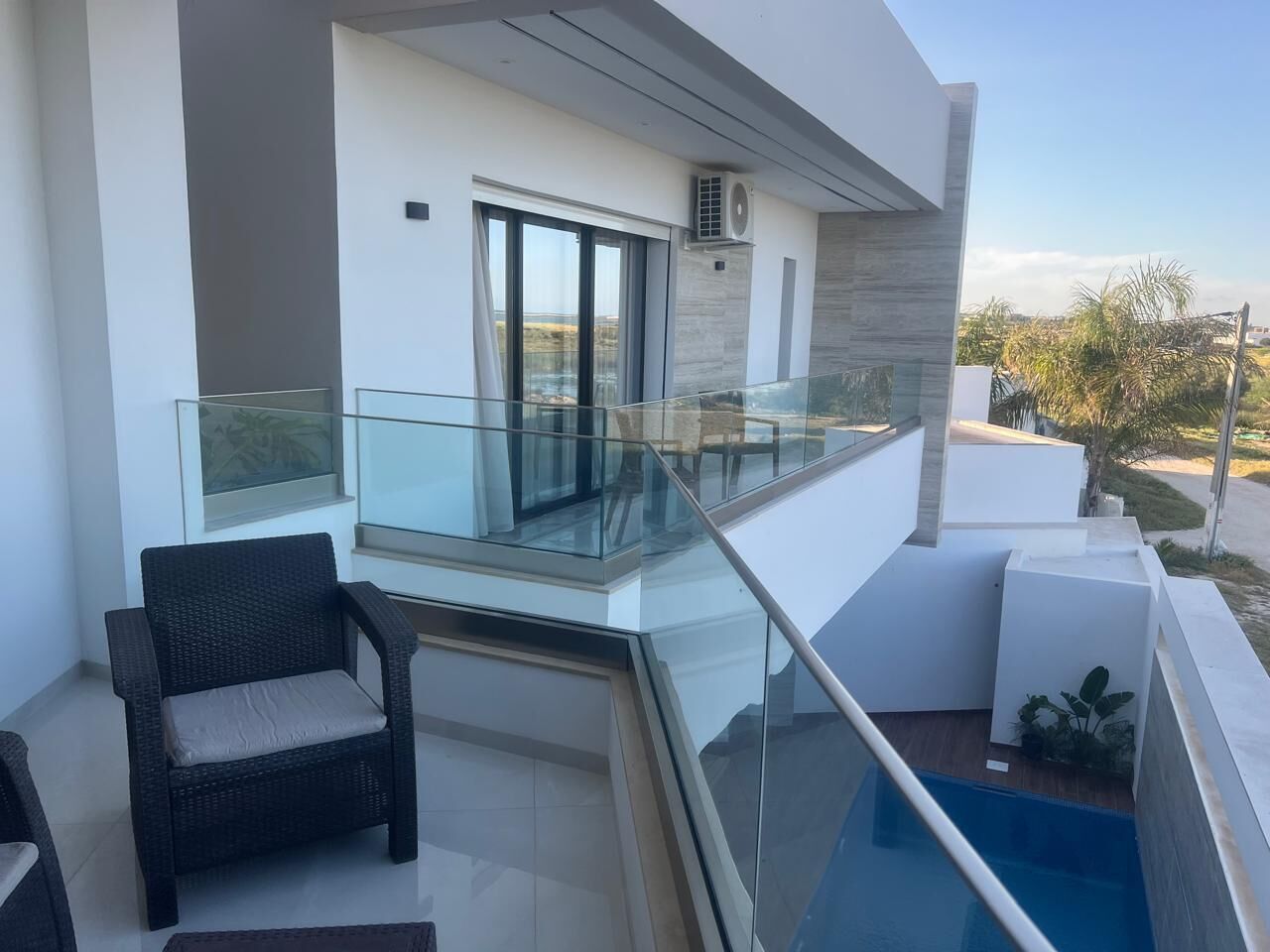 Ein moderner Balkon mit Glastrennwand, einem Korbstuhl und einem kleinen Pool.