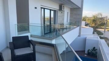 A modern balcony with a glass railing, a wicker chair, and a small pool.