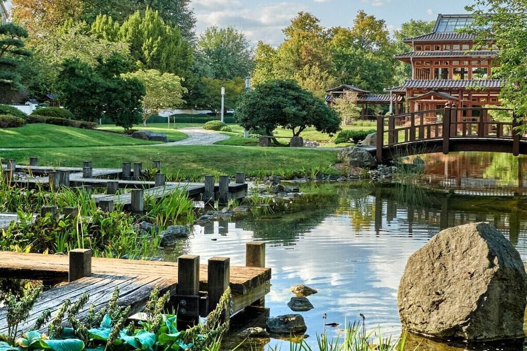 A traditional Japanese garden with a wooden bridge, a pond, and a pagoda-style building.