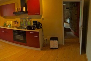 A compact kitchen with red cabinets, a built-in oven, a coffee maker, and a small white appliance on the floor. - Holiday apartment with 2 bedrooms (Bad Langensalza)