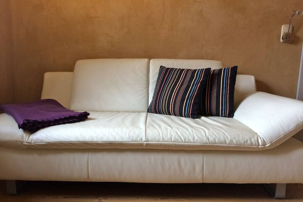 Un canapé en cuir blanc, agrémenté d’un plaid violet et de coussins à rayures, est placé devant un mur à texture.