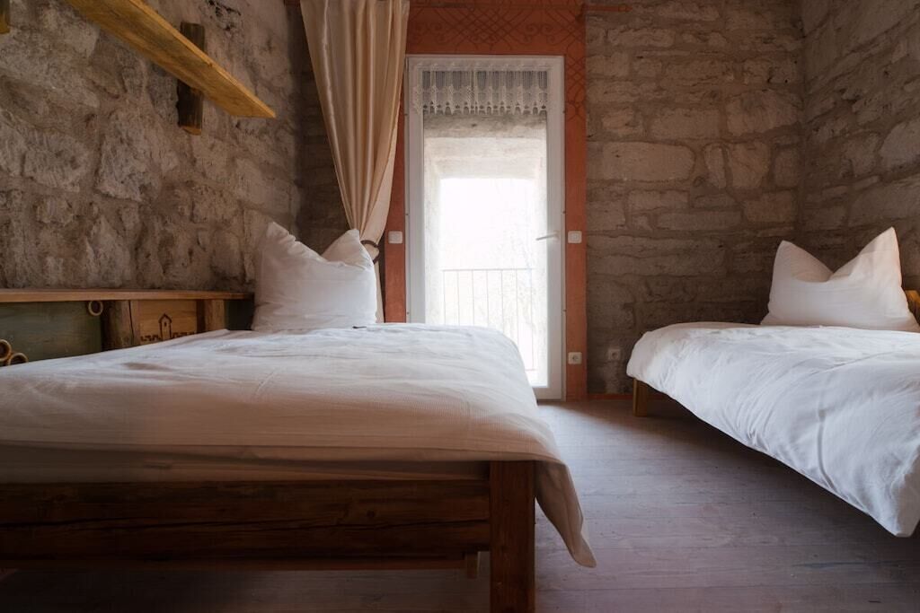 A bedroom with two beds, a wooden headboard, a stone wall, and a door leading to a balcony.