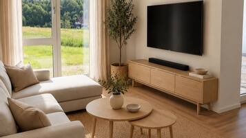 Ein modernes Wohnzimmer mit einer Couch, einem Couchtisch, einem Fernseher und Blick auf eine grüne Landschaft durch große Fenster.