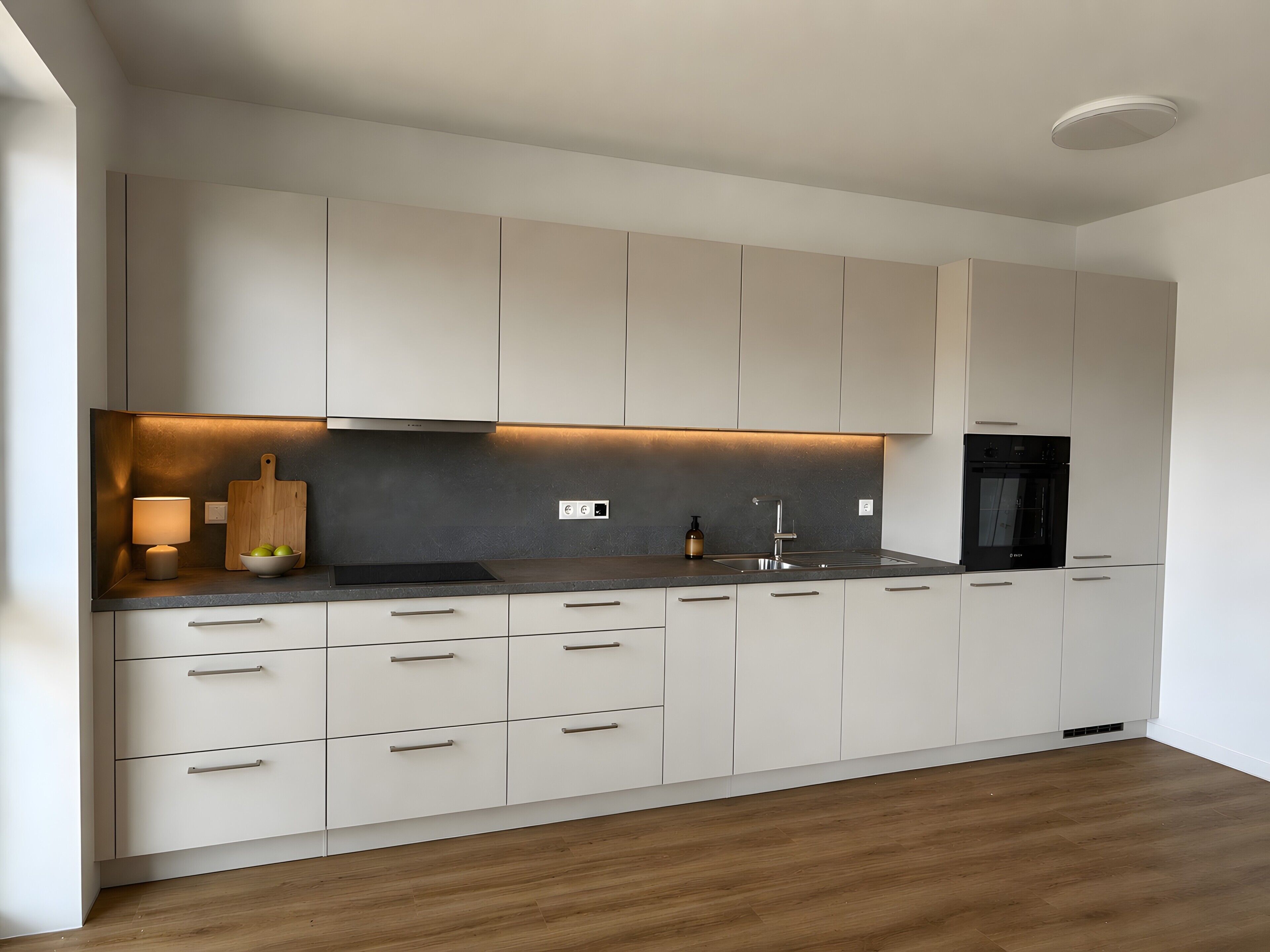 Eine moderne Küche mit weißen Schränken, einer schwarzen Arbeitsplatte und einem eingebauten Backofen.