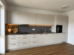 A modern kitchen with white cabinets, a black countertop, and a built-in oven.