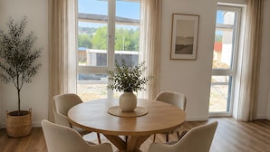Een eetgedeelte met een ronde houten tafel, zes stoelen, een kamerplant en een geweven vloerkleed.
