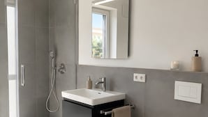 Een moderne badkamer met een douchecabine van glas, een wit wastafelmeubel met spiegel en een toilet.