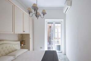 Ein Schlafzimmer mit einem Bett, einem Kleiderschrank, einer Chandelieber und einer Glastür zu einem Balkon.