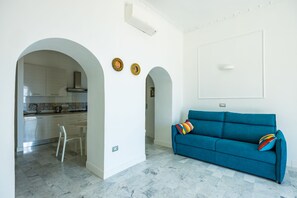 Ein modernes Wohnzimmer mit einem blauen Sofa und einem durch einen Bogen sichtbaren Küchenbereich.