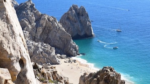A coastal landscape with rocky cliffs, a sandy beach, and clear blue water. - Cozy Cabo Condo 2br, Shared Pool, Gated Community, 20 Walk to Beach (Cabo San Lucas)