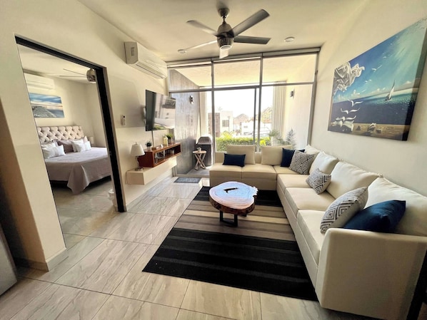 A modern living room with a sofa, coffee table, and a television. - Cozy Cabo Condo 2br, Shared Pool, Gated Community, 20 Walk to Beach (Cabo San Lucas)