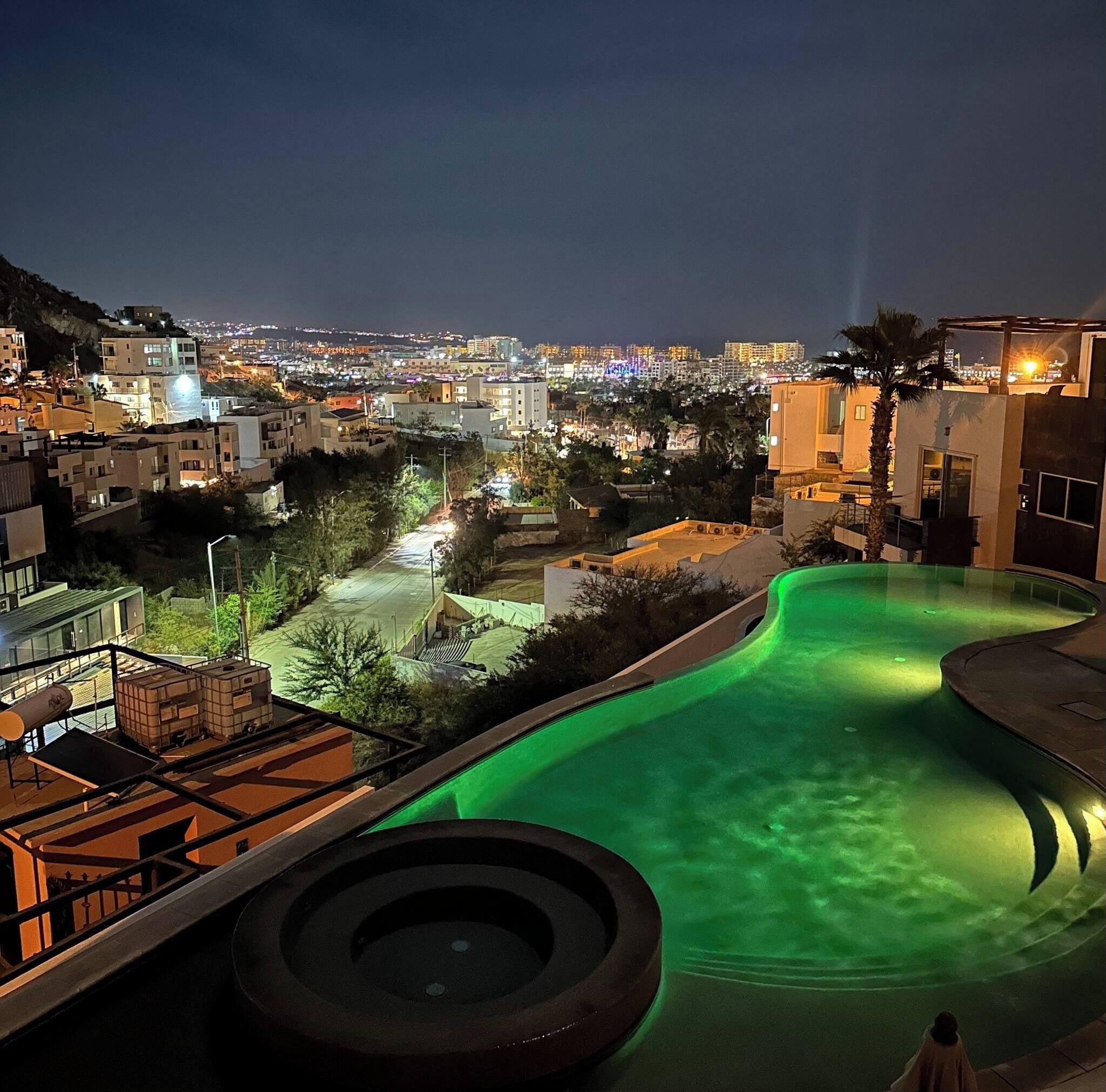 A swimming pool with a curved design, surrounded by buildings and a view of a cityscape at night.