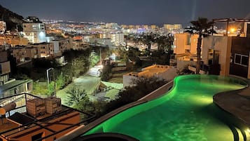 A swimming pool with a curved design, surrounded by buildings and a view of a cityscape at night.