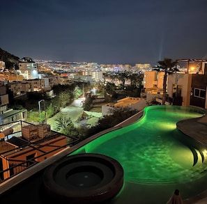 Una piscina de diseño curvo, rodeada de edificios y con vistas a un paisaje urbano nocturno.