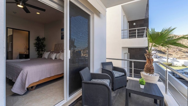A balcony with a bed, two chairs, a small table, and a potted plant. - Cozy Cabo Condo 2br, Shared Pool, Gated Community, 20 Walk to Beach (Cabo San Lucas)