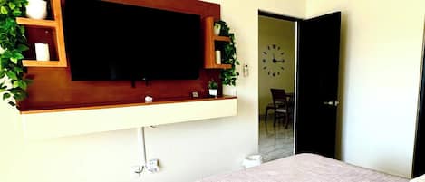 Un dormitorio con cama, ventilador de techo, televisor montado y puerta que da a otra habitación.