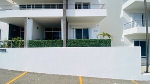 A multi-story building with a white facade, a balcony on the upper floor, and a hedge in front. - Cozy Cabo Condo 2br, Shared Pool, Gated Community, 20 Walk to Beach (Cabo San Lucas)