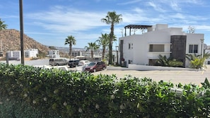 A modern building with a parking lot, surrounded by greenery and palm trees. - Cozy Cabo Condo 2br, Shared Pool, Gated Community, 20 Walk to Beach (Cabo San Lucas)