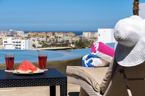 A seaside view with a table set for two, featuring a watermelon and two drinks. - Cozy Cabo Condo 2br, Shared Pool, Gated Community, 20 Walk to Beach (Cabo San Lucas)