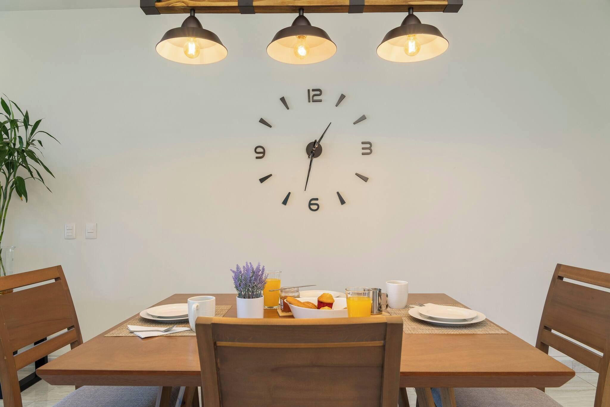 A dining area with a wooden table, chairs, a wall clock, and a plant.