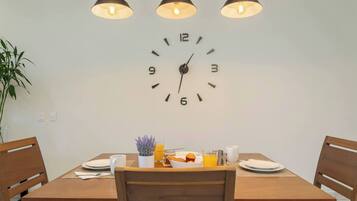 A dining area with a wooden table, chairs, a wall clock, and a plant.