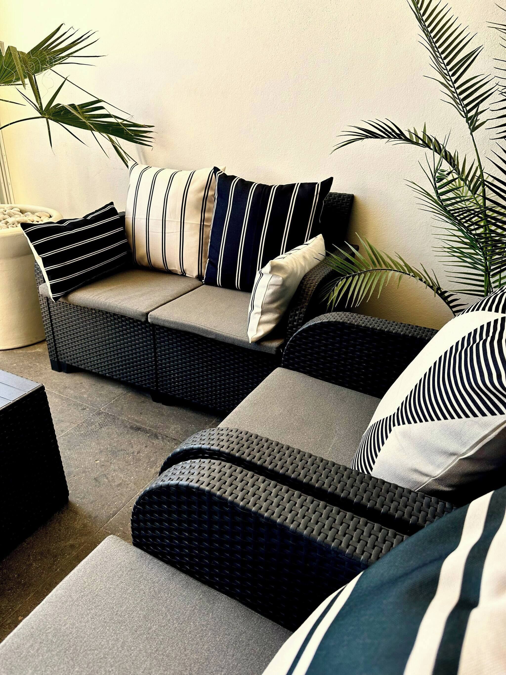 A sectional sofa with striped cushions, a woven chair, and a potted plant.