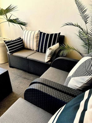 A sectional sofa with striped cushions, a woven chair, and a potted plant. - Cozy Cabo Condo 2br, Shared Pool, Gated Community, 20 Walk to Beach (Cabo San Lucas)