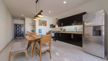 Una cocina moderna con un refrigerador de acero inoxidable, gabinetes negros y un comedor con sillas y mesa de madera.