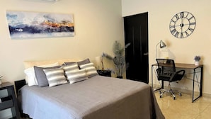 A bedroom with a bed, a desk, a chair, a clock, and a painting on the wall. - Cozy Cabo Condo 2br, Shared Pool, Gated Community, 20 Walk to Beach (Cabo San Lucas)
