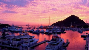 A marina at sunset with multiple boats docked, a prominent mountain in the background, and a clear sky. - Cozy Cabo Condo 2br, Shared Pool, Gated Community, 20 Walk to Beach (Cabo San Lucas)