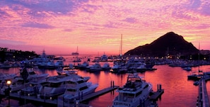 Un puerto deportivo al atardecer con varias embarcaciones amarradas, una montaña destacada al fondo y cielo despejado.