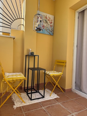 A corner room with yellow walls, a black metal table, two yellow folding chairs, a white rug, and a birdcage with a hanging light. - Your Sunny Getaway in Spain - Casa de Palmeras (Cancelada)